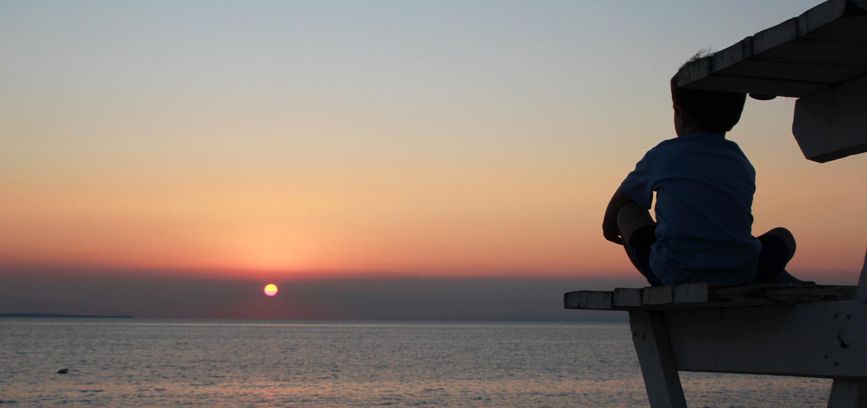 a boy looking at a beach sunset